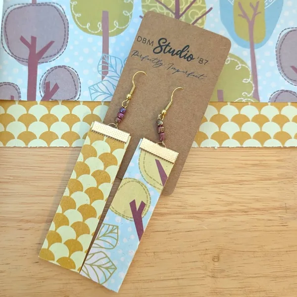 Larger rectangle dangle scrapbook paper earrings with gold metal accents and purple/blue irridescent beads. Front is light blue with trees and back is gold/yellow fan shaped. Front and back are shown.